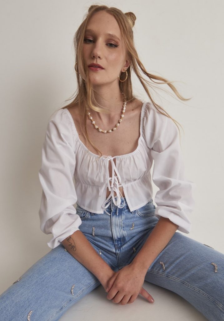 Cloud Dancer: looks com a cor de 2026 Menina branca, com cabelo semi preso, vestindo blusa estilo bata com, com três amarrações frontais. Produto com a cor cloud Dancer, a cor de 2026